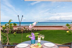 A table set for two with a bottle of wine, glasses, and a plate of food, overlooking a beach with a clear sky.