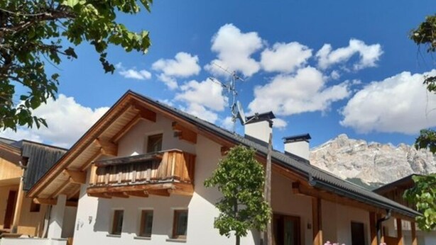 A traditional chalet with a balcony, a stone staircase, and a mountain backdrop. - Apartment Raisc - your home in Val Badia (La Villa)