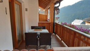 A balcony with wooden railings, a table with chairs, and a view of mountains. - Apartment Raisc - your home in Val Badia (La Villa)