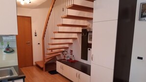 A kitchen with wooden flooring, white cabinets, a black countertop, and a wooden staircase. - Apartment Raisc - your home in Val Badia (La Villa)