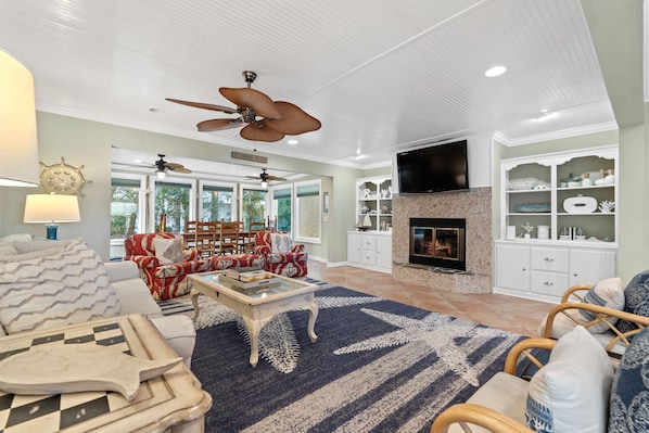A spacious living room with a fireplace, ceiling fans, and a large TV.
