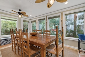 A dining area with a wooden table and chairs, large windows, and a ceiling fan.