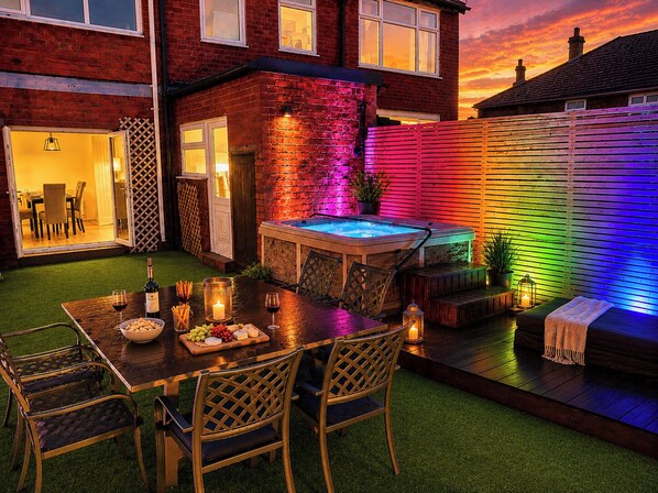 A backyard with a hot tub, a dining table with chairs, and a small seating area. - Family Modern 3 Bedroom hot tub House (Blackpool)