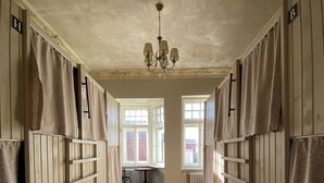 Un couloir doté d’un plancher en bois, d’un lustre et de grandes fenêtres ornées de rideaux.