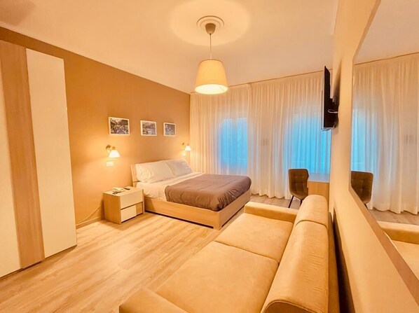 A modern bedroom with a bed, bedside tables, a sofa, and a TV mounted on the wall.