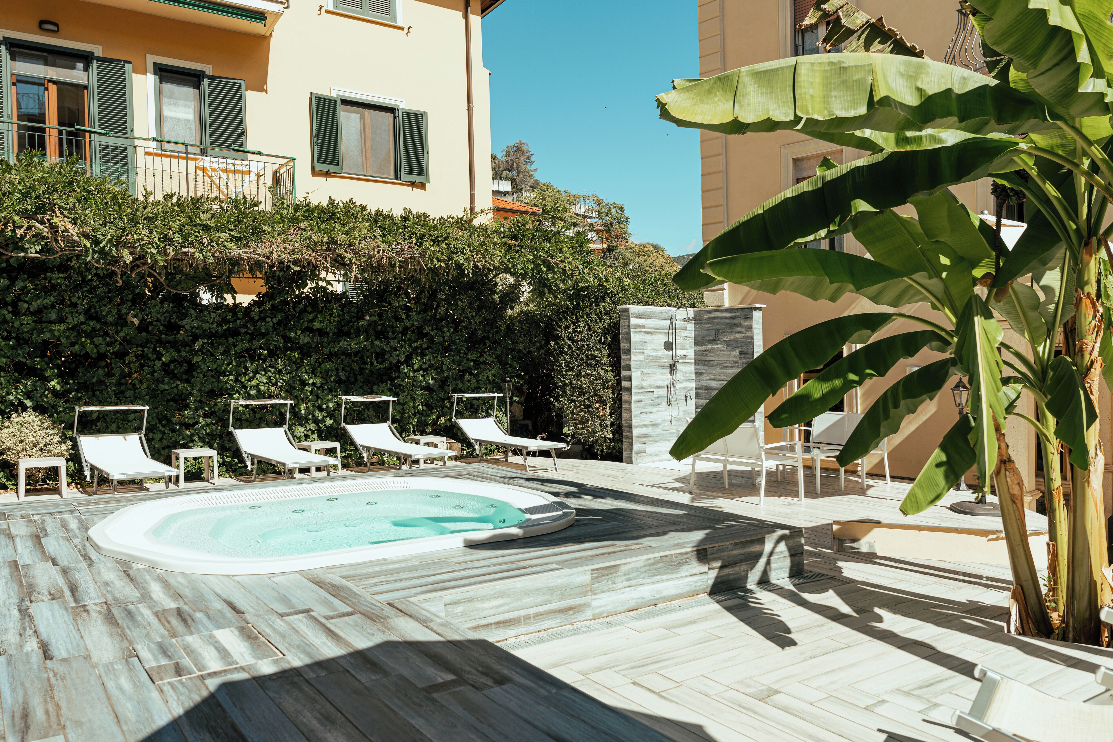 Area piscina con sedie a sdraio, vasca idromassaggio e vista su un edificio con balconi.