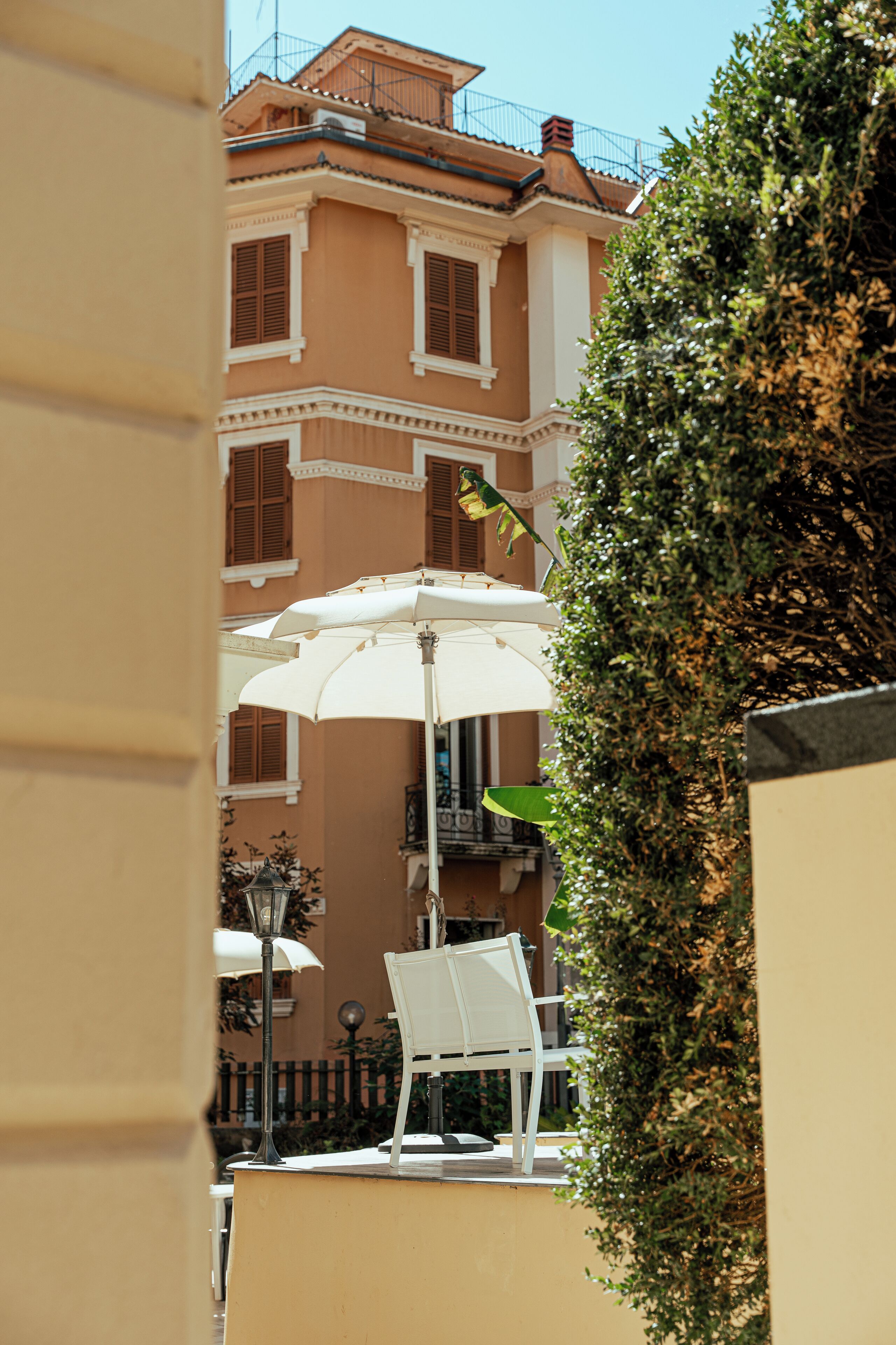 A white outdoor seating area with a table and chairs, an umbrella, and a building in the background.