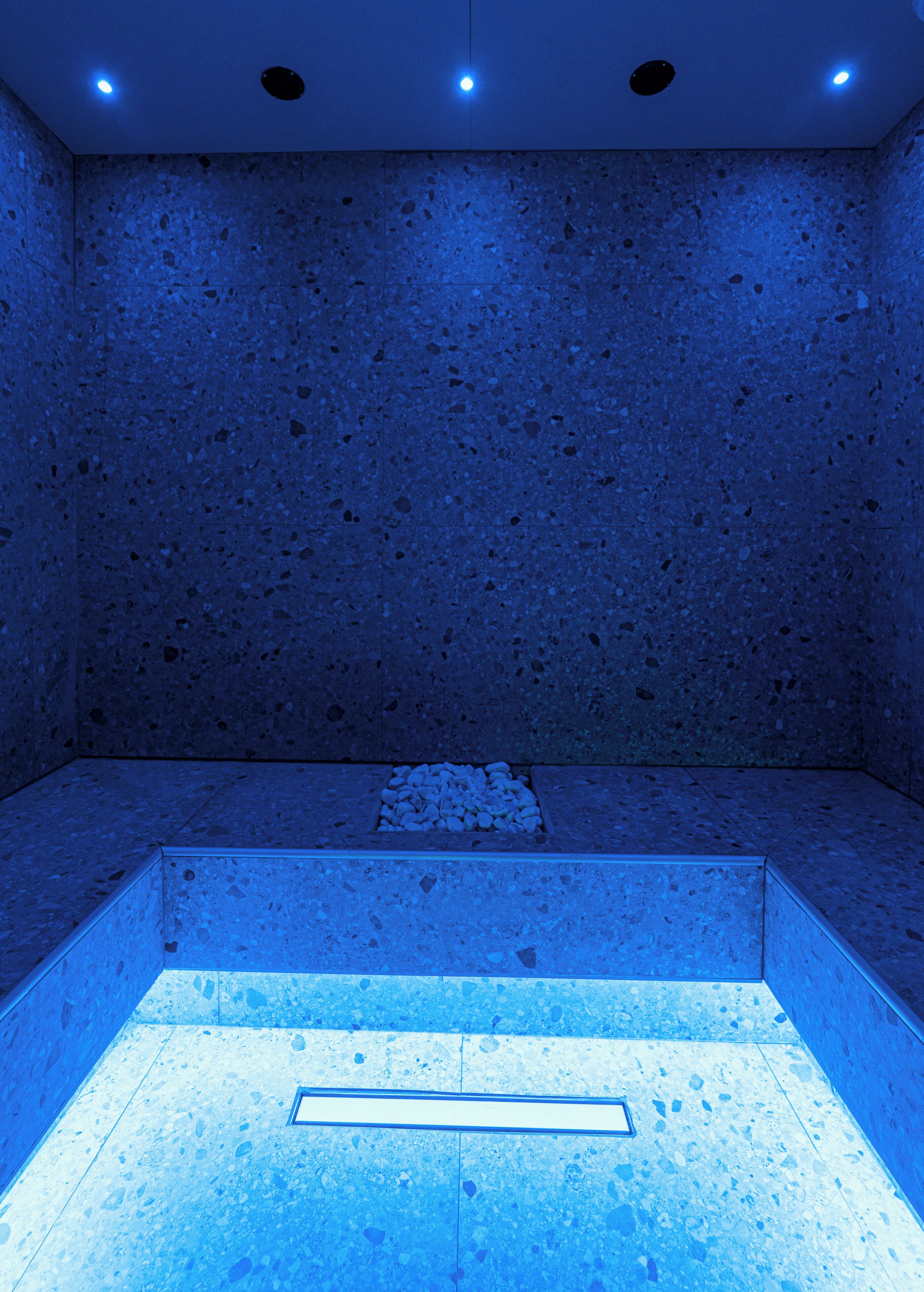 Un cuarto de spa con suelo y paredes de tono azul, una zona de estar rectangular e iluminación empotrada en el techo.