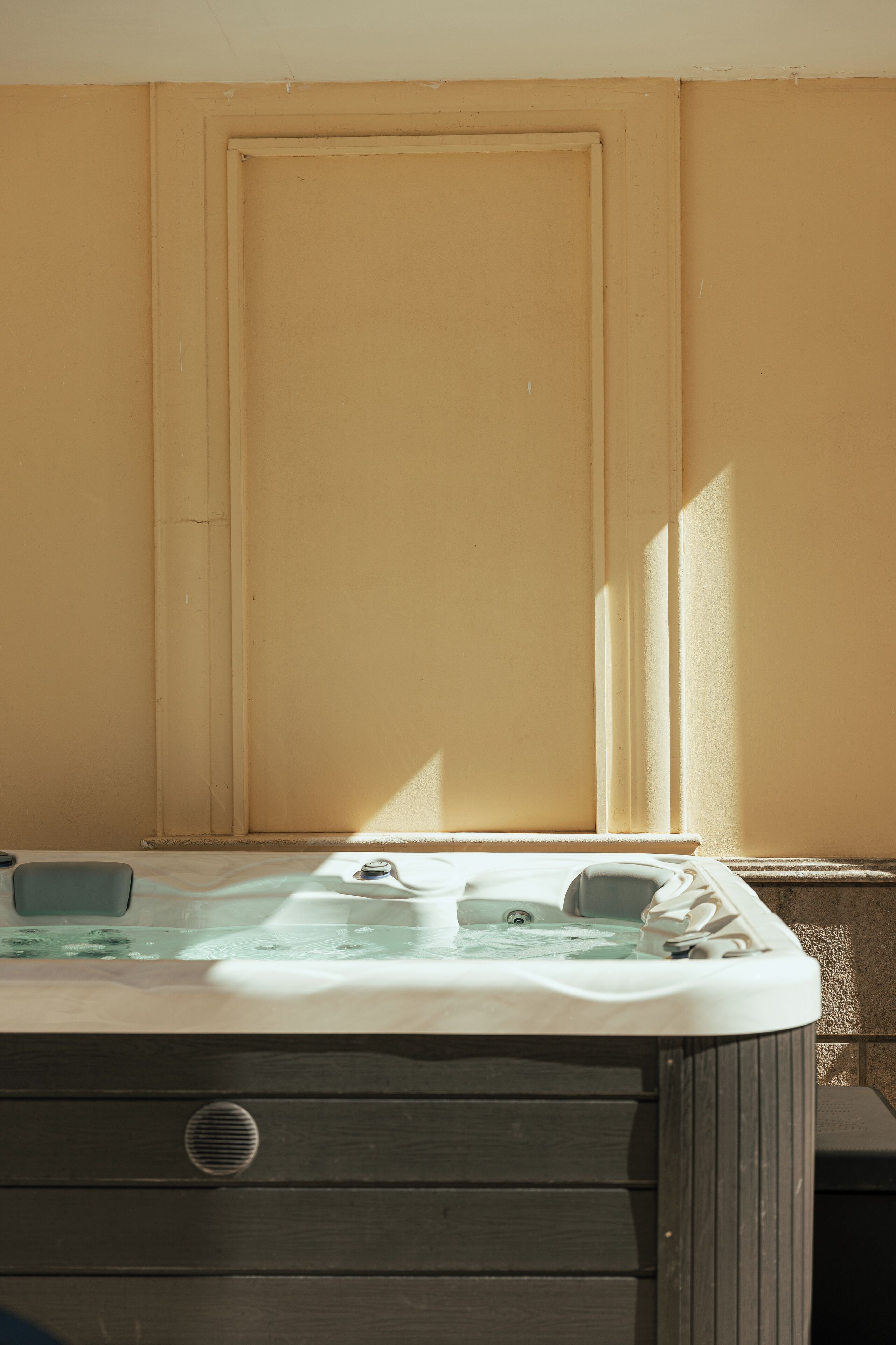 Un jacuzzi con base de madera, ubicado frente a una pared beige con una puerta.