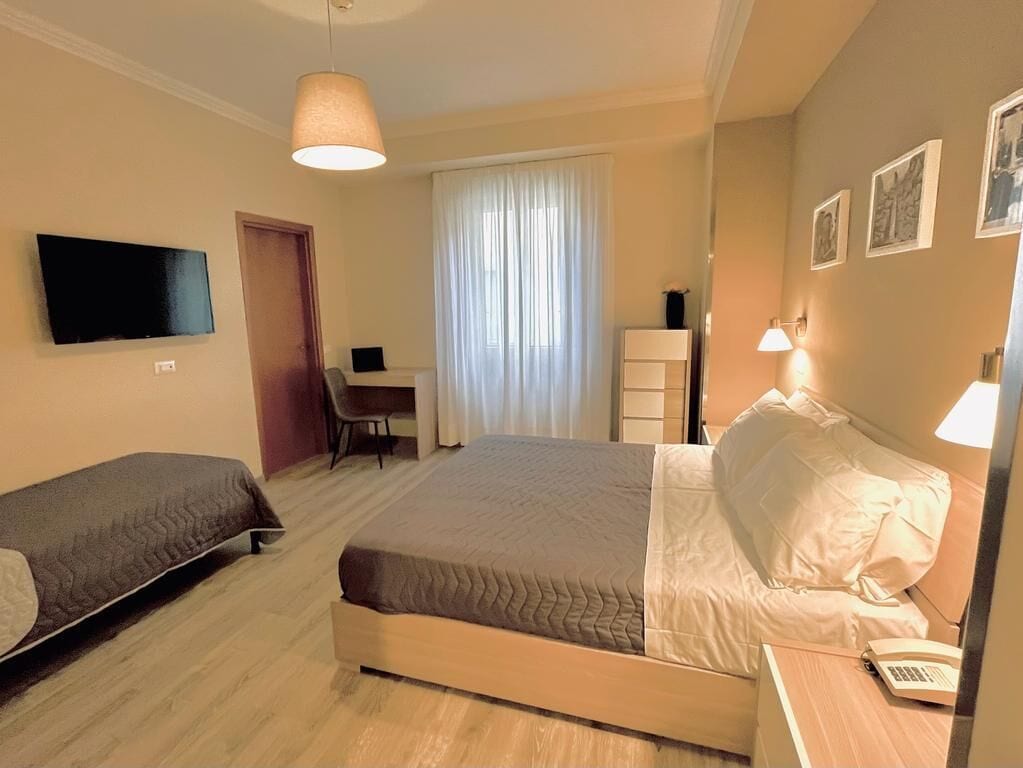 A hotel room with a bed, a desk, a chair, a TV, and a lamp.