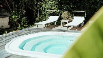 Ein Whirlpool mit zwei Liegestühlen, umgeben von Grün.
