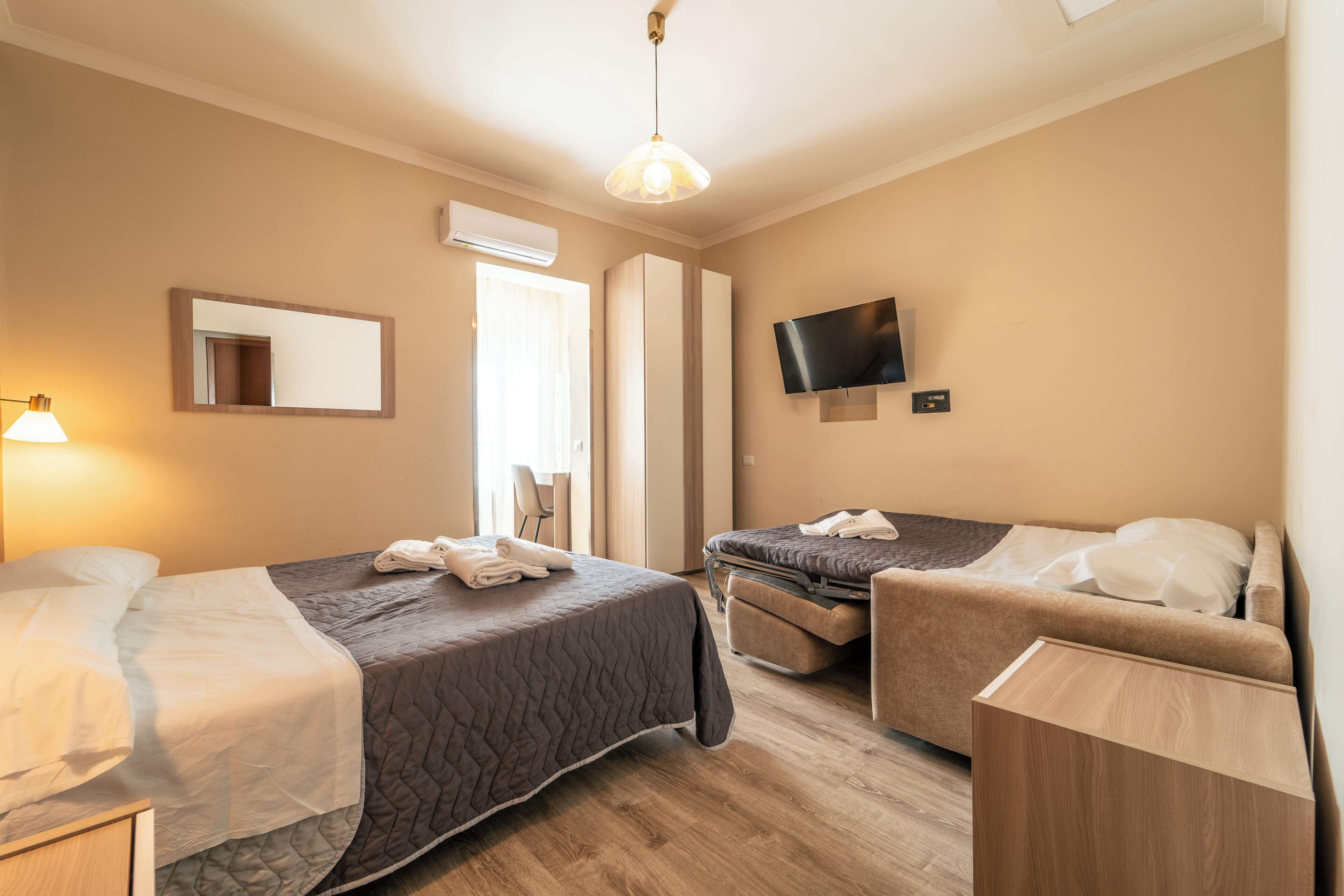 A hotel room with two beds, a TV, a mirror, and a window.