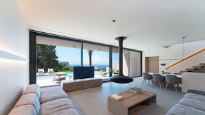 A modern living room with a large window, a flat-screen TV, a sofa, a coffee table, and a staircase. - Casa Palmera, Casa Palmera (Rhodes)