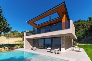 Une maison moderne à deux étages, dotée d’une piscine, de grandes baies vitrées et d’une façade en pierre.