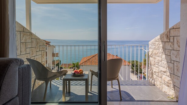 A balcony with a table set with fruit, wicker chairs, and a view of the sea. - Villa Miki (Podstrana)