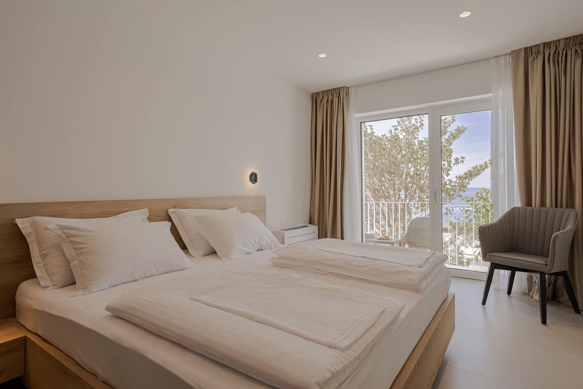 A bedroom with a large bed, a chair, and a view of the outdoors.