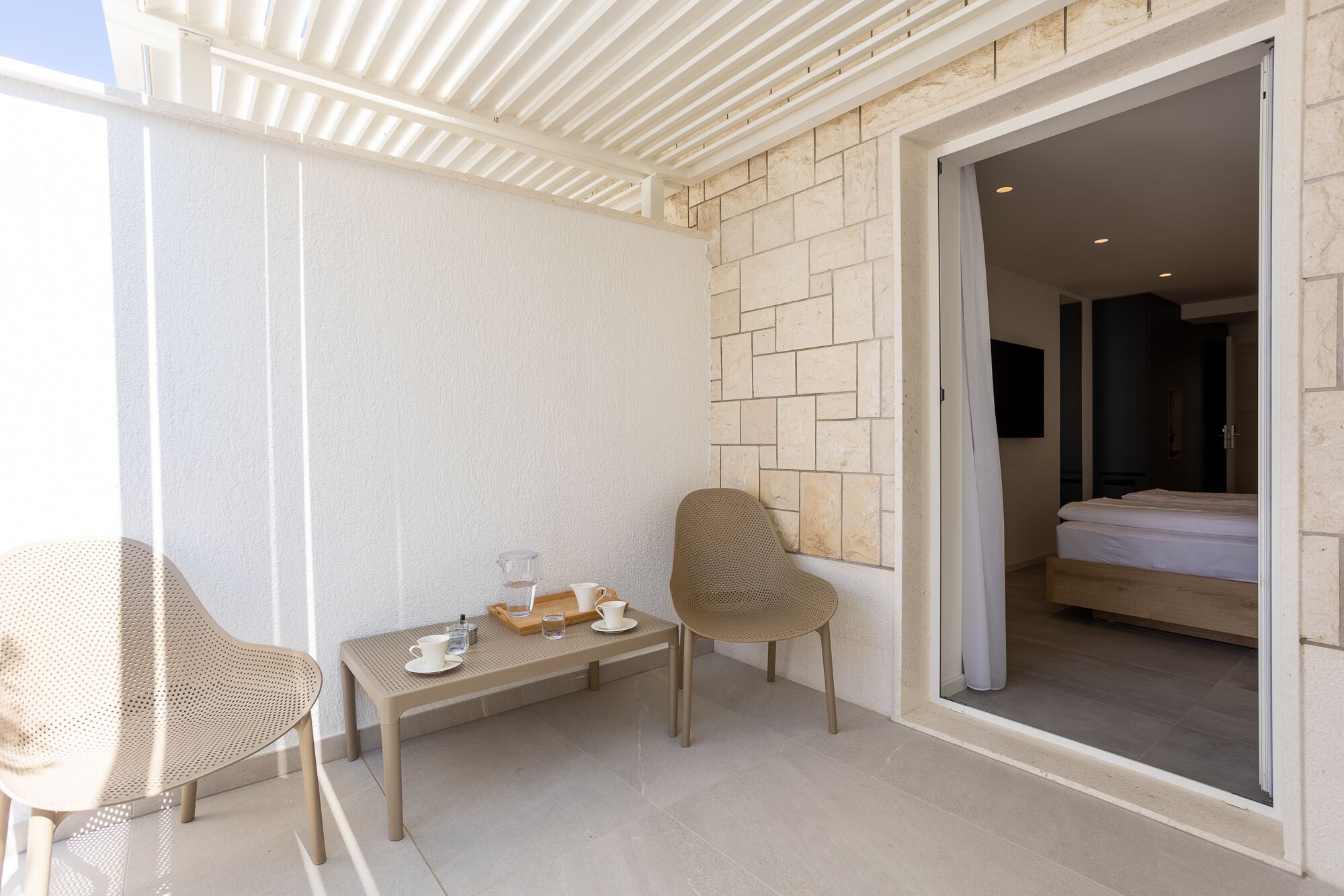 A balcony with a table, two chairs, and a bed visible through an open door.