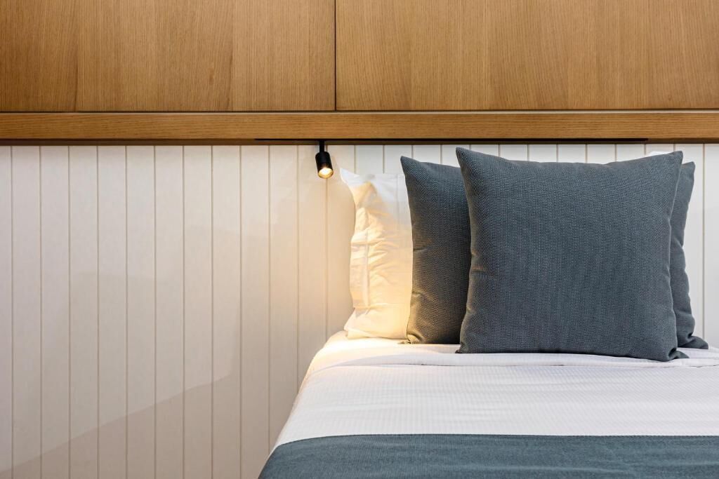 Een bed met twee kussens, een houten hoofdbord en een wand met verticale lijnen.
