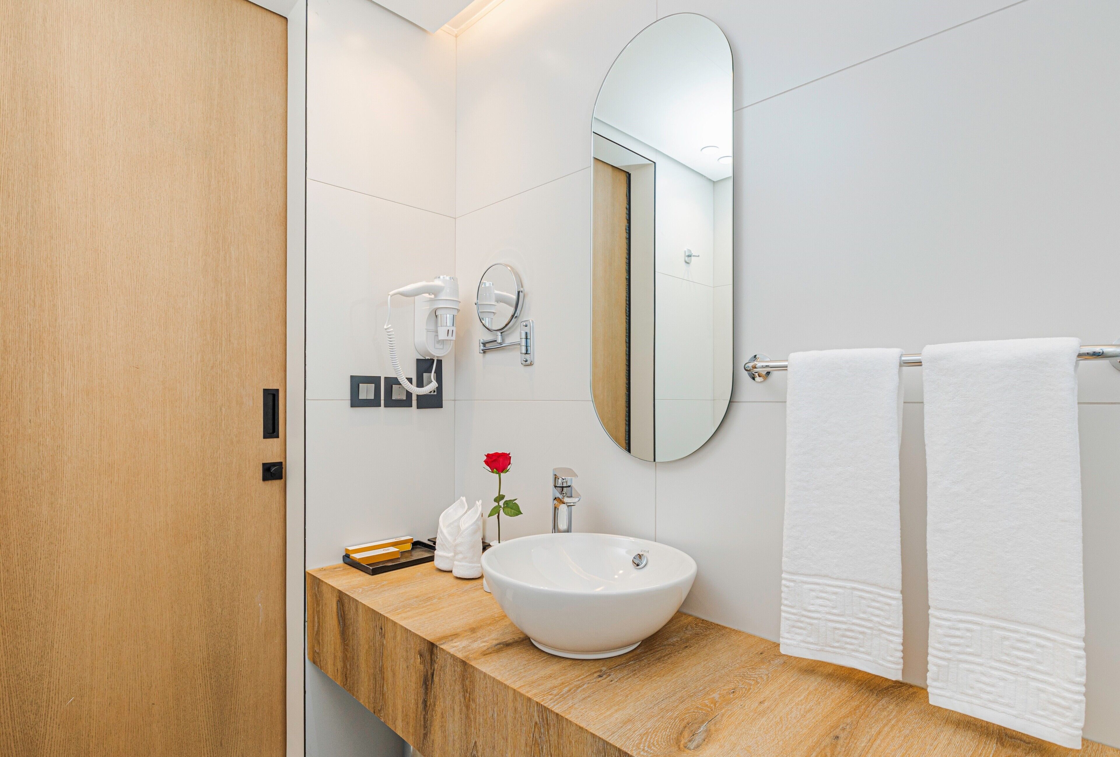 Un baño moderno con tocador de madera, un lavamanos blanco, un espejo y un perchero para toallas.