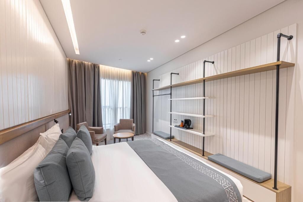 Ein modernes Hotelzimmer mit einem großen Bett, einer Sitzecke und integrierten Regalen.
