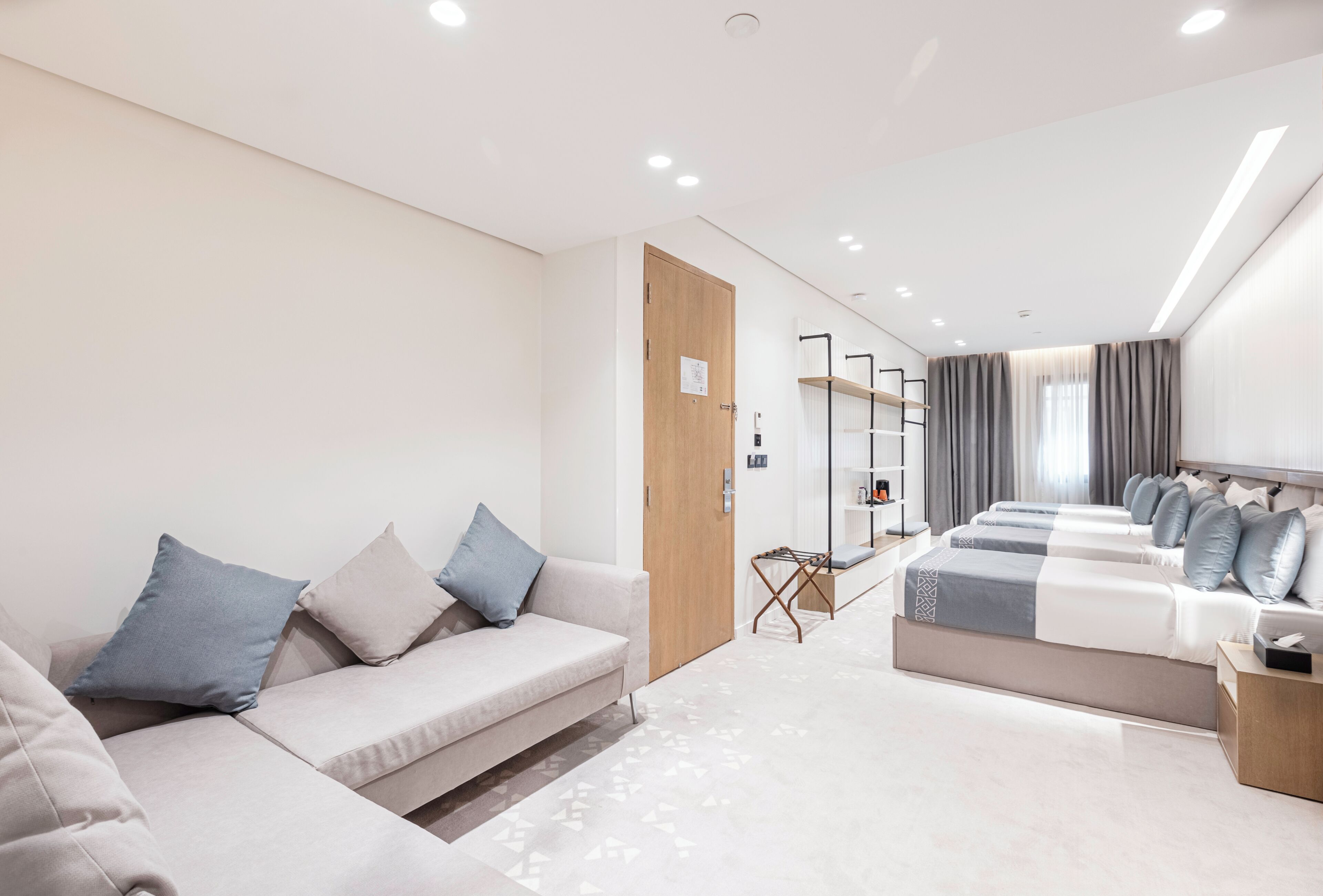 Ein modernes Hotelzimmer mit einer Couch, einem Bett mit vielen Kissen, einer Holztür und einem Fenster mit Vorhängen.