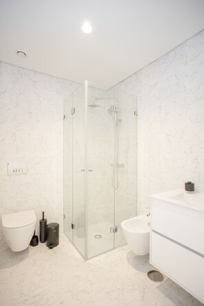 Un bagno moderno con doccia vetrata, WC bianco, bidet e mobile lavabo bianco con specchio.