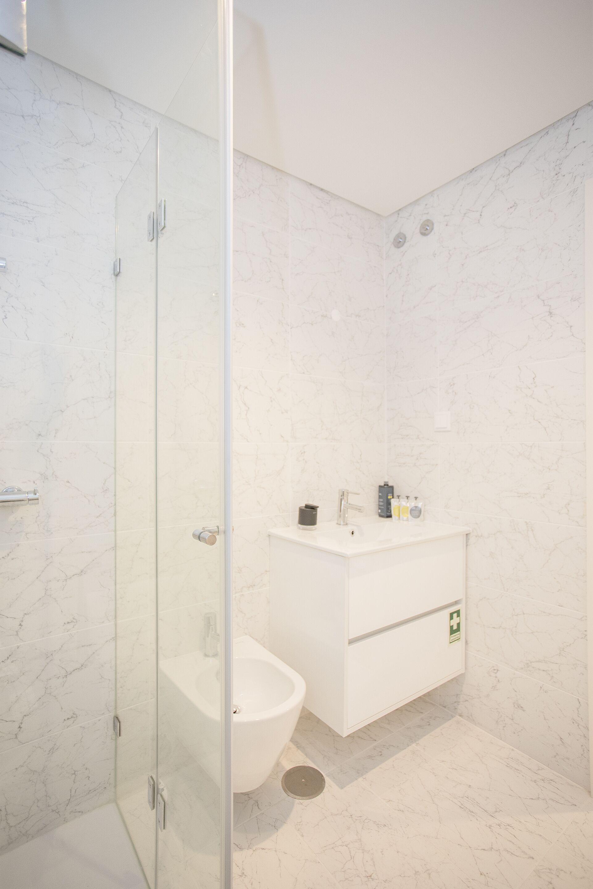 A modern bathroom with a glass-enclosed shower, a white sink, and a marble-tiled wall.