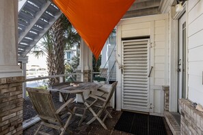 An outdoor patio with a wooden table and chairs, a white door, and a covered area with a slatted roof. - Sound Side Studio Apartment with Boat Slip (Bridgeview on Broad) (Beaufort)