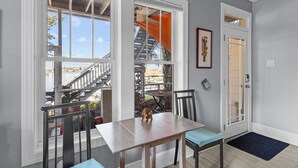 Un espace repas comprenant une table et des chaises, une vue sur un balcon doté d’une balustrade, et une porte avec un panneau en verre.