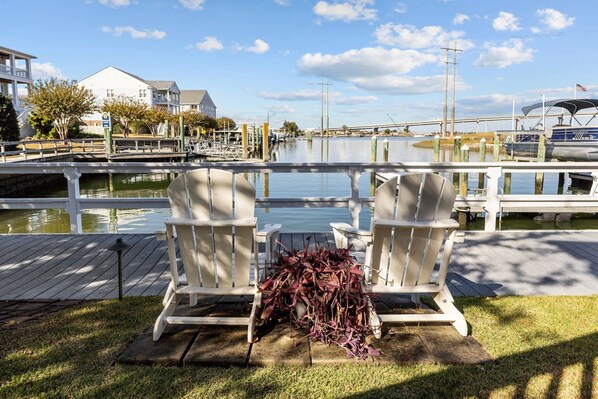 A dock with two Adirondack chairs and a table, a wooden deck, and a marina with boats and a bridge in the background. - Sound Side Studio Apartment with Boat Slip (Bridgeview on Broad) (Beaufort)