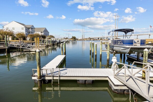 A marina with docked boats, a wooden pier, and a white building with a gray roof.