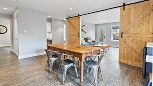 Um quarto espaçoso com uma grande mesa de jantar de madeira, cadeiras de metal e uma porta de celeiro deslizante.
