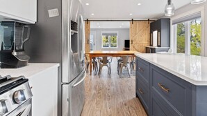 Uma cozinha moderna com uma ilha central, eletrodomésticos de aço inoxidável e um espaço de jantar com mesa e cadeiras de madeira.