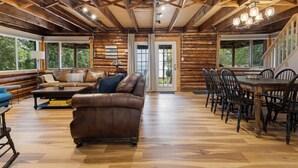 A log cabin interior with a wooden dining table, leather sofa, and large windows. - Skipping Rock Cottages: Ultimate Lakeside Retreat (Meaford)