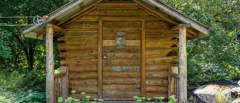 A rustic wooden cabin with a front porch, surrounded by lush greenery.