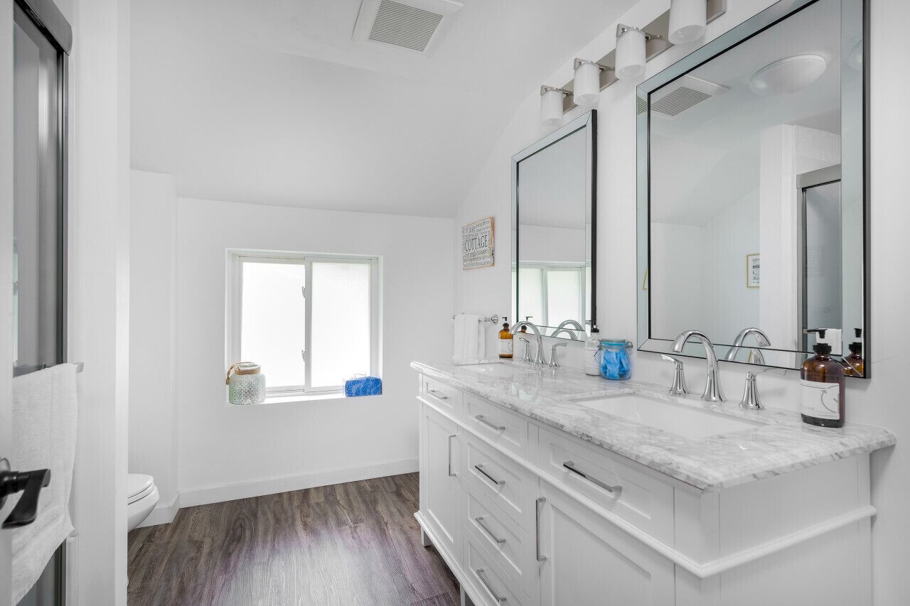A modern bathroom with a large mirror, two sinks, and a window.
