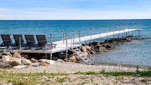 A pier with lounge chairs and a staircase leading to a rocky shoreline.