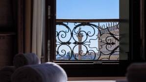 A hotel room with a bed, rolled towels, and a view of a balcony with wrought iron railings. - 286 Piazza San Marco (Venice)