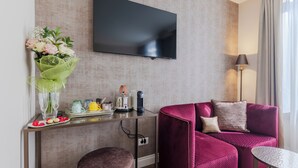 A modern living room with a flat-screen TV, a pink sofa, a small round table, a coffee machine, and a bouquet of flowers on a console table. - 286 Piazza San Marco (Venice)
