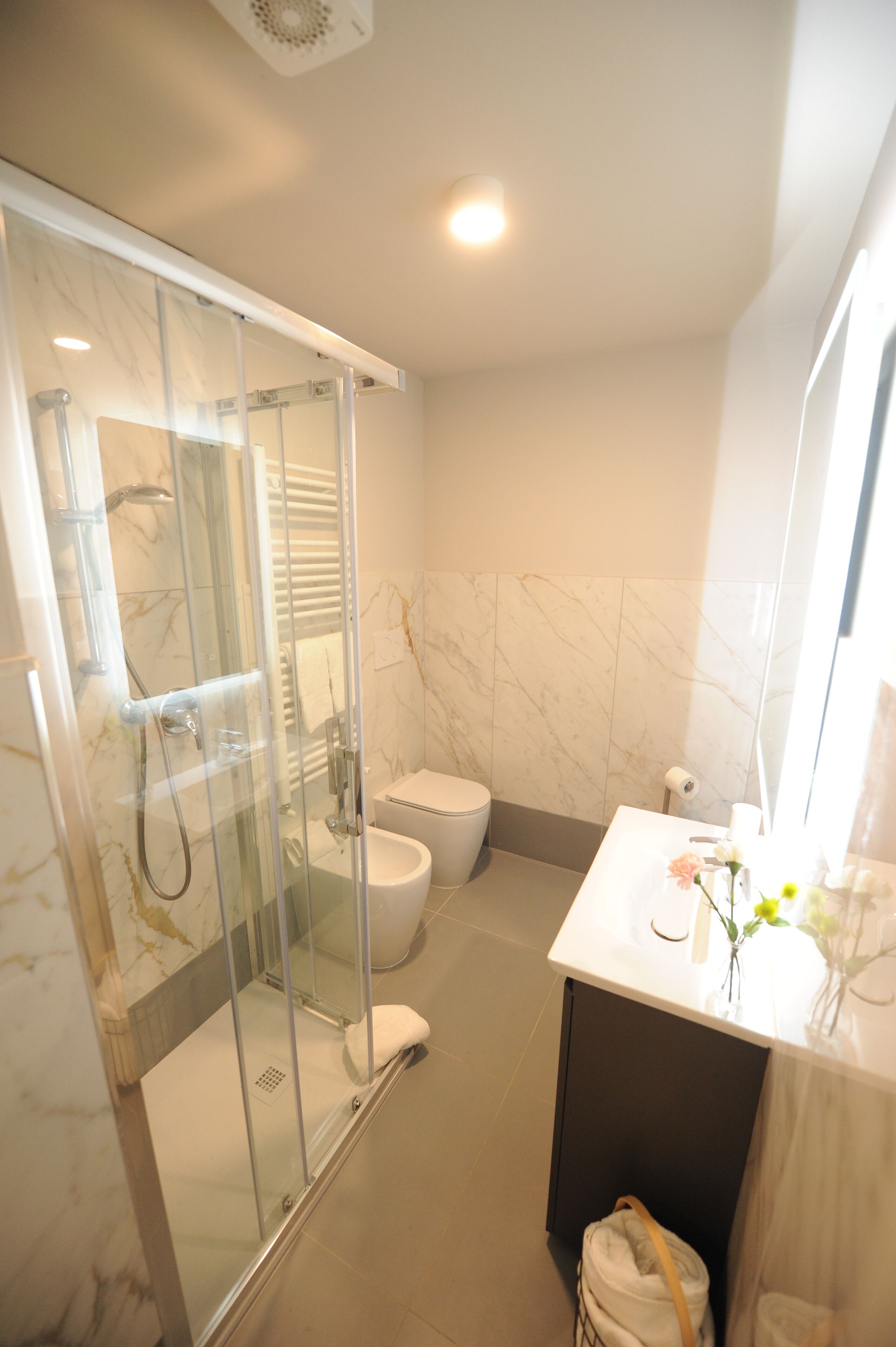 A bathroom with a glass-enclosed shower, a toilet, and a sink with a vase of flowers.