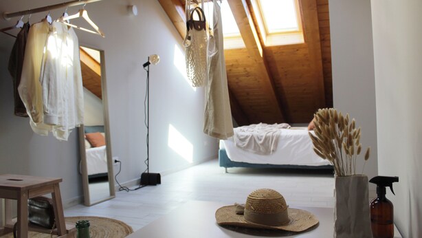 Quarto com teto inclinado, uma cama, luminária pendente, espelho e janela.