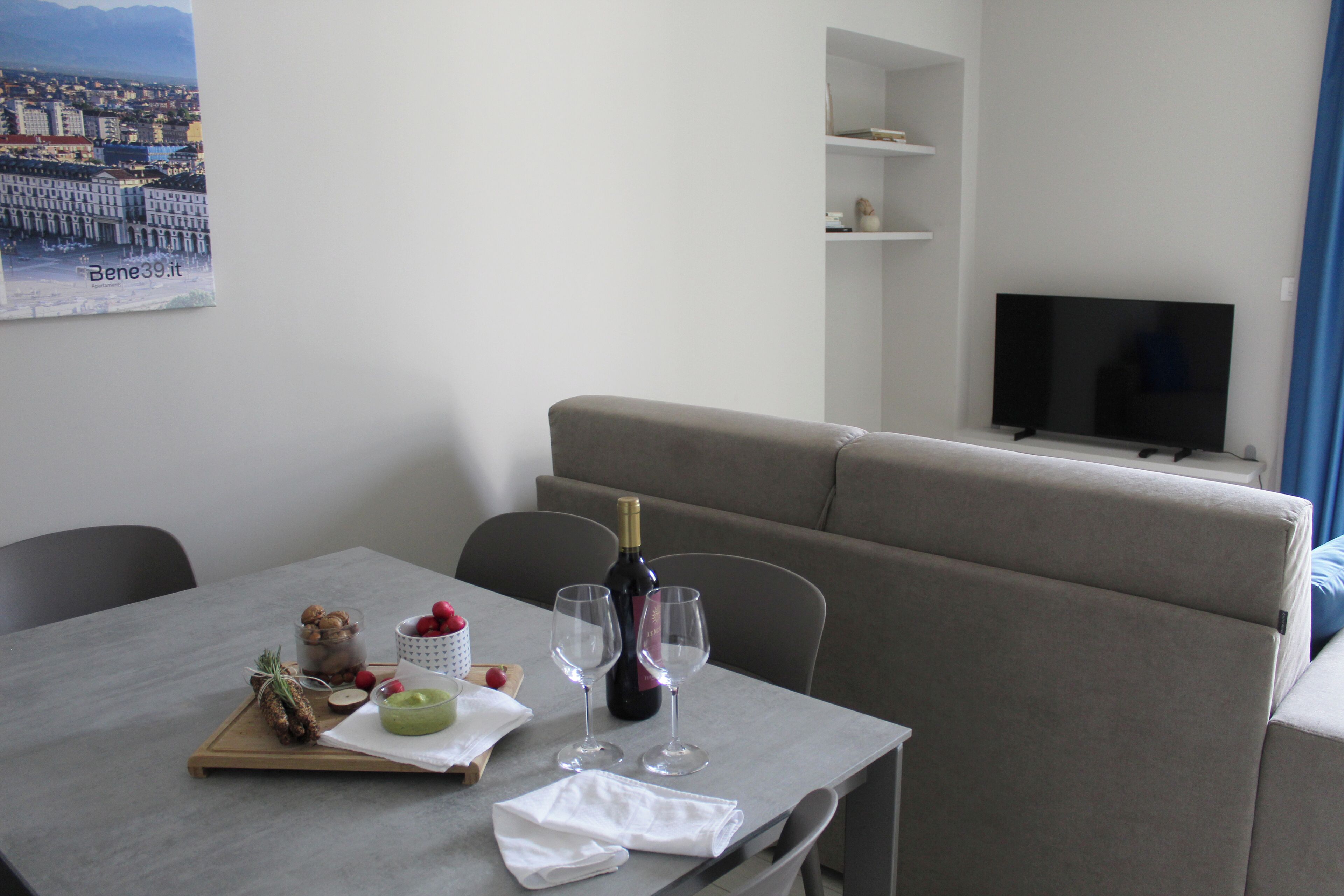 A hotel room with a dining table set for two, a bottle of wine, and a tray with food and drinks.
