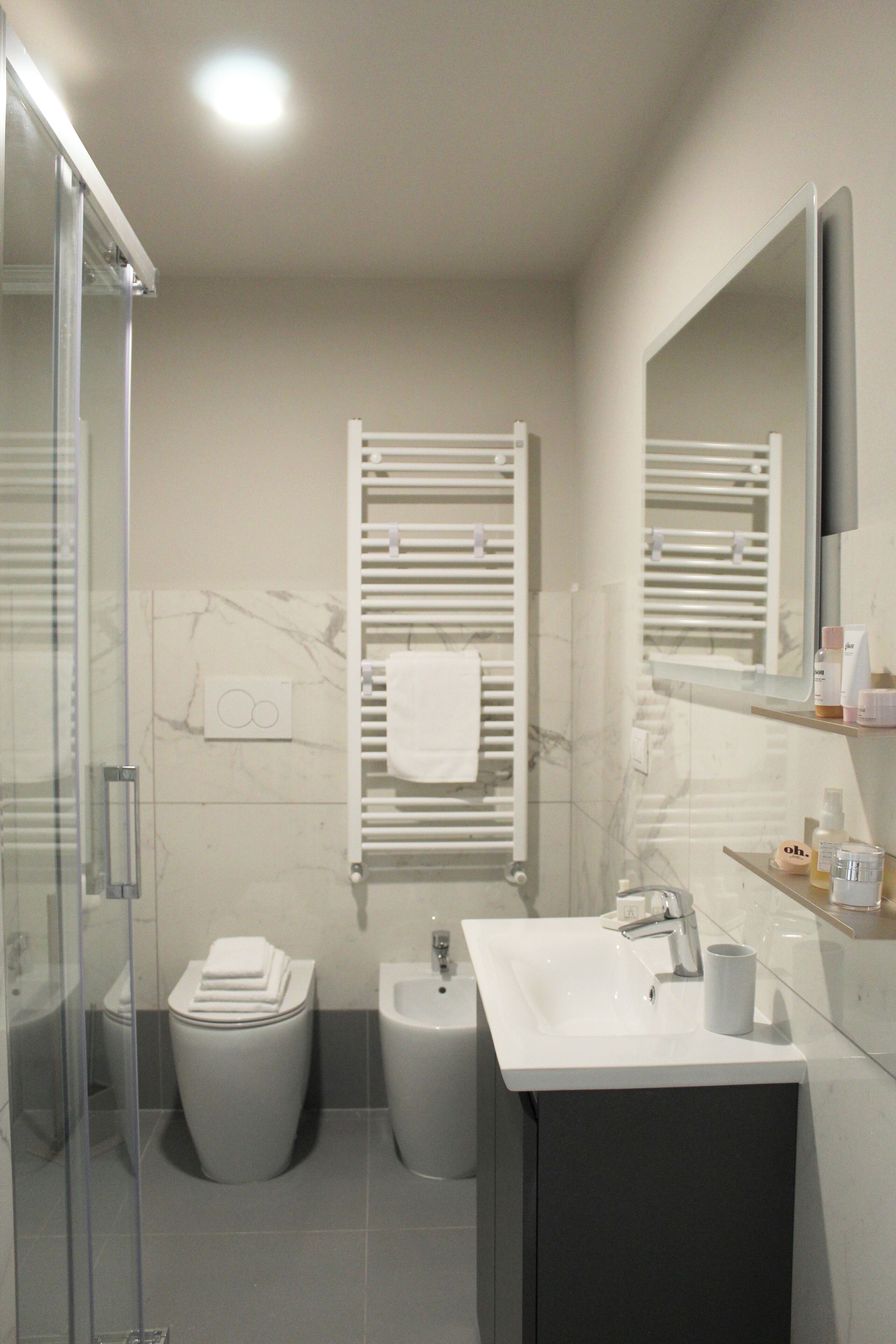 Un bagno moderno con box doccia in vetro, un water, un bidet, un lavabo con specchio e un portascopevoli.