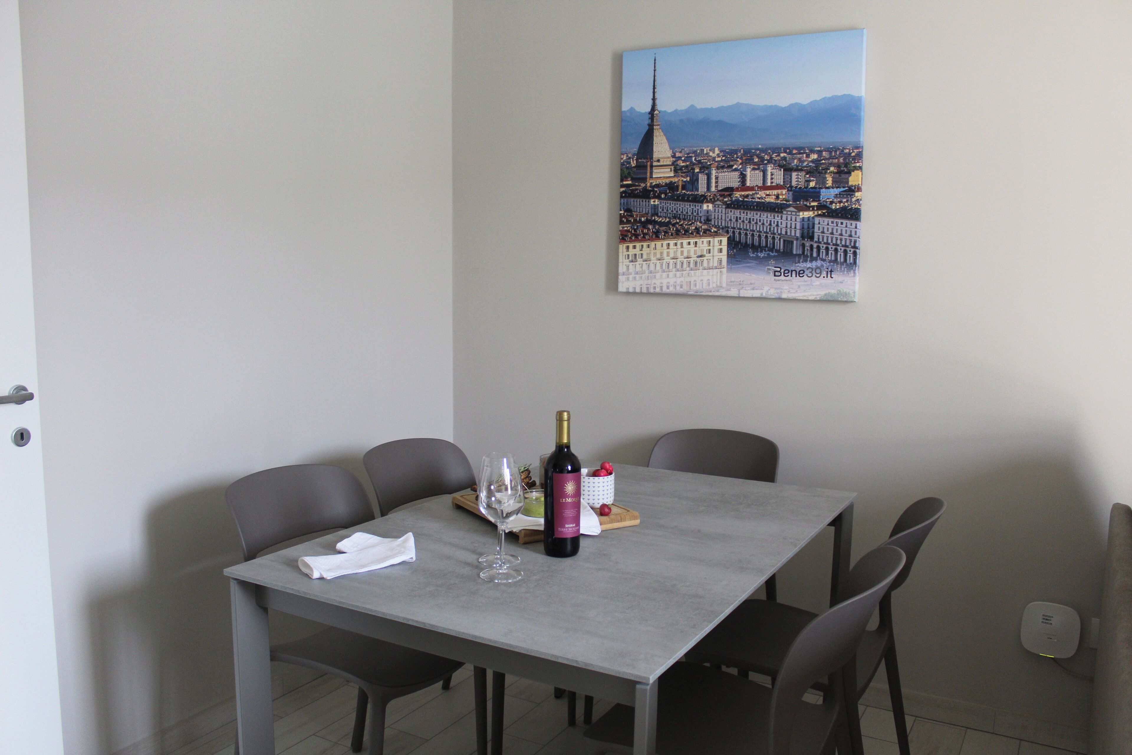 Un tavolo da pranzo con una bottiglia di vino, bicchieri e una piccola ciotola di frutta.