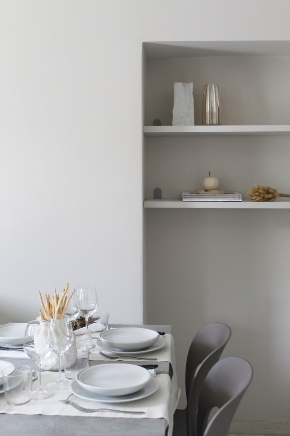 A dining table set with plates, glasses, and cutlery, with a vase of dried flowers and a candle on a shelf above. - BENE 39 (Turin)