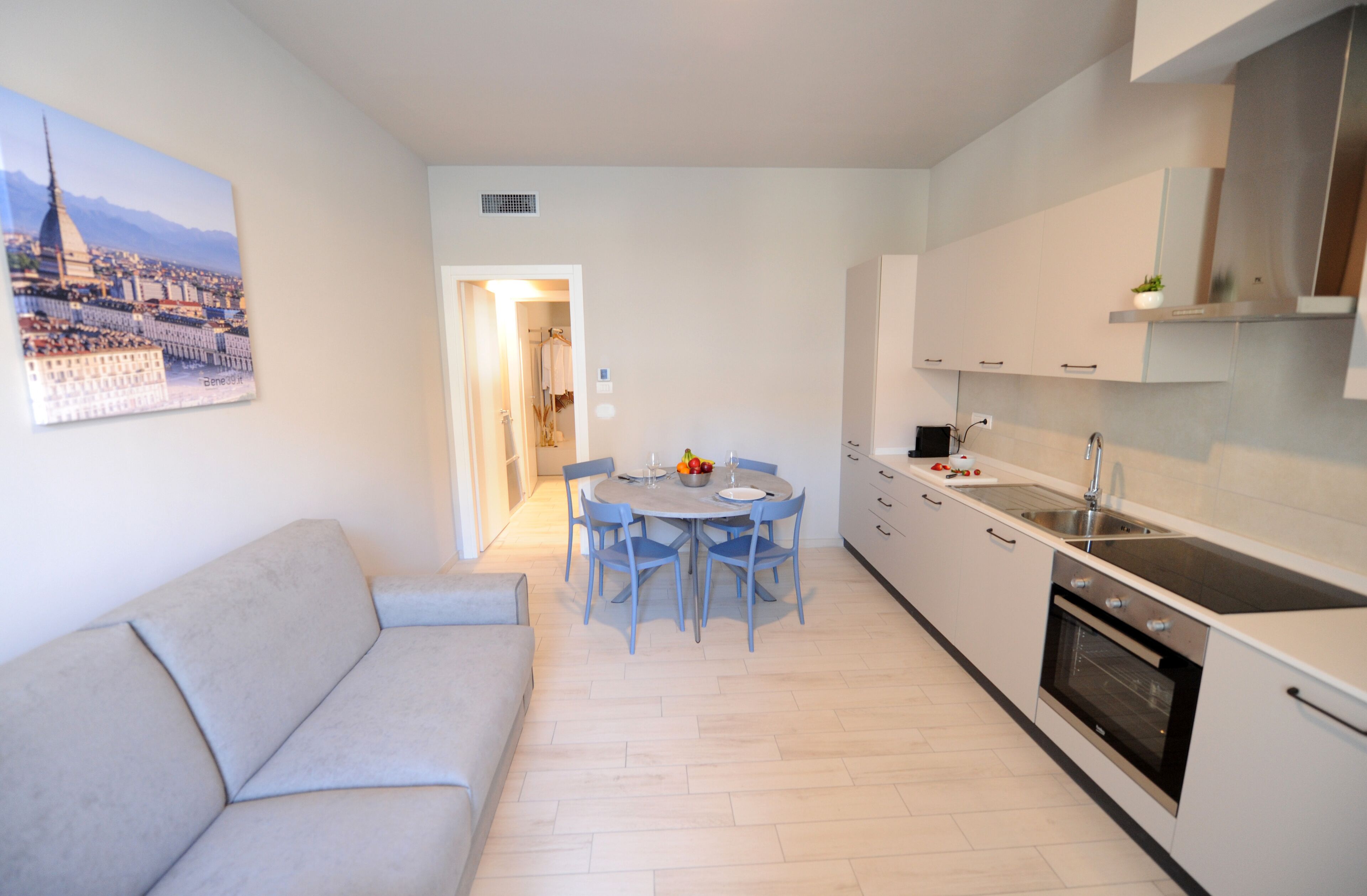A modern kitchen with a dining area, a sofa, and a cityscape painting on the wall.