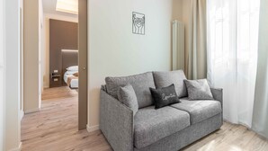A modern living room with a grey sofa, a small black pillow with the word "Essential," and a minimalist wall art piece.