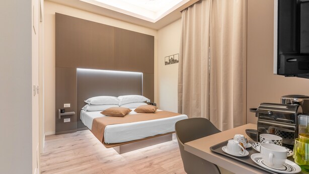 A modern hotel room with a bed, bedside tables, a desk with a coffee maker, and a TV.