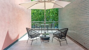 A patio area with two black wire-framed chairs, a round table, and a large beige umbrella.
