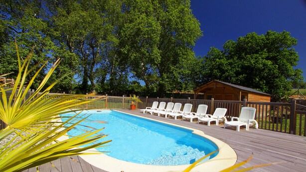 Una terraza de madera con piscina, rodeada de sillones blancos y una cabaña de madera.